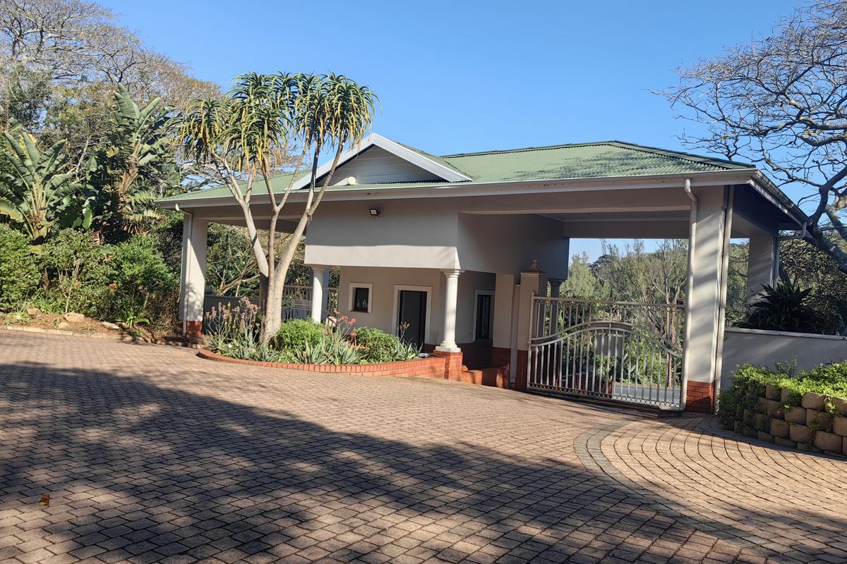 A well-maintained residential entrance featuring a paved driveway, covered portico, and secure metal gate set within a landscaped garden.
