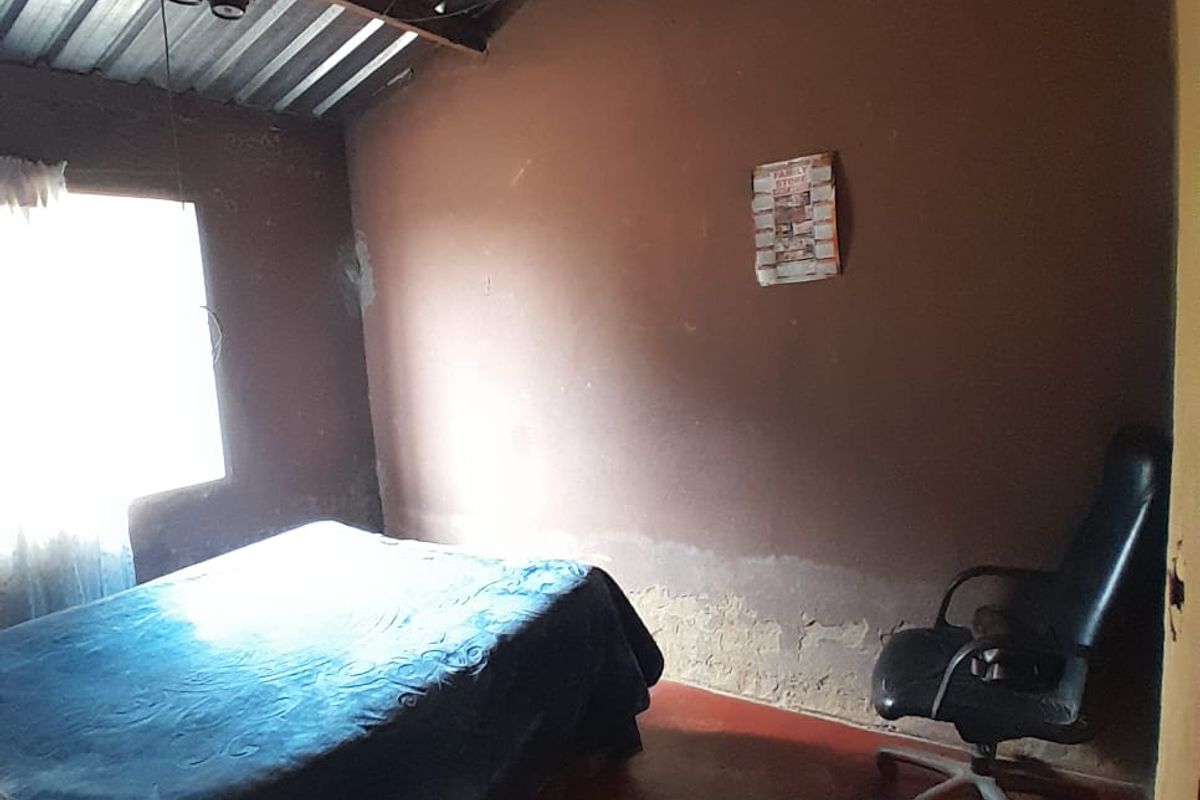A bedroom featuring exposed corrugated metal roofing, painted concrete flooring, and visible wall deterioration requiring maintenance and cosmetic updates.