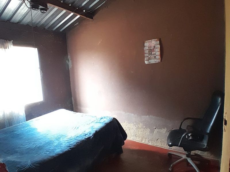 A bedroom featuring exposed corrugated metal roofing, painted concrete flooring, and visible wall deterioration requiring maintenance and cosmetic updates.