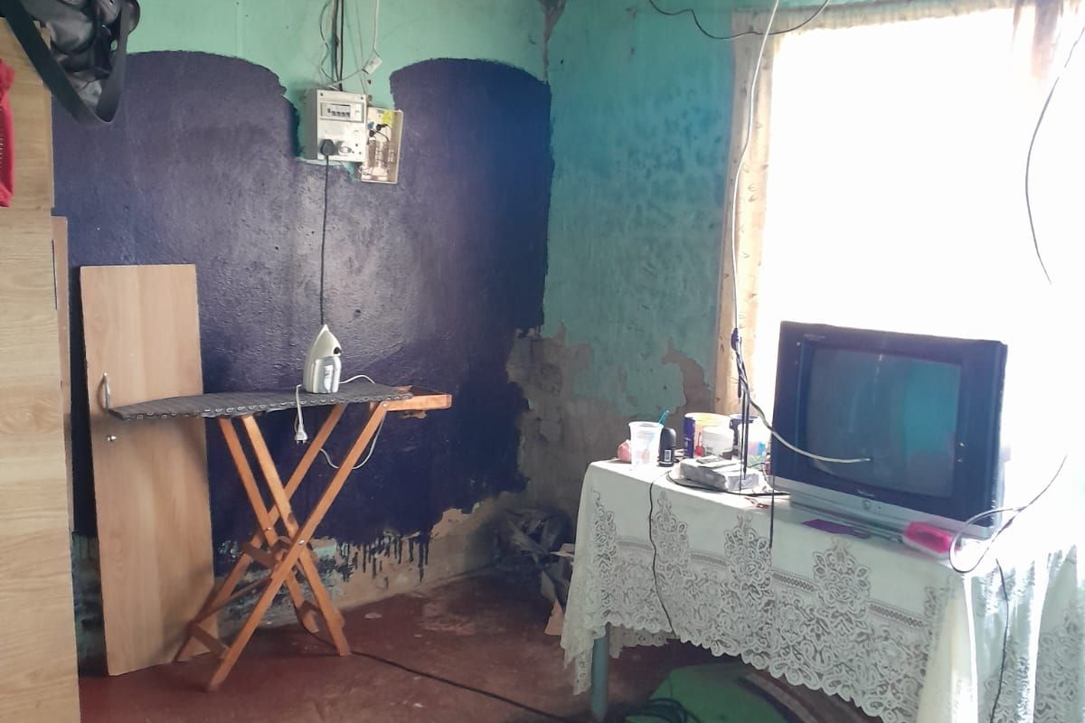 A living area featuring exposed corrugated metal roofing, concrete flooring, and significant wall surface deterioration requiring repair and renovation.