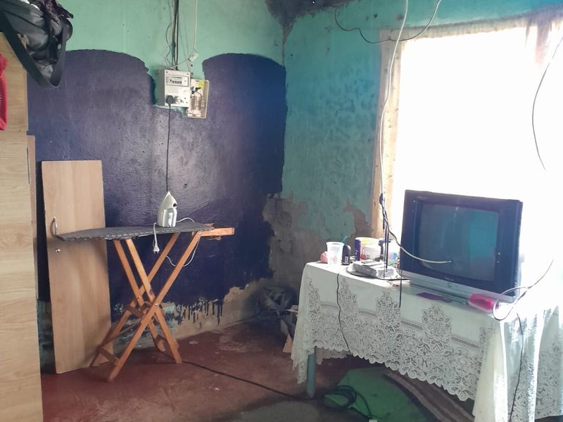 A living area featuring exposed corrugated metal roofing, concrete flooring, and significant wall surface deterioration requiring repair and renovation.