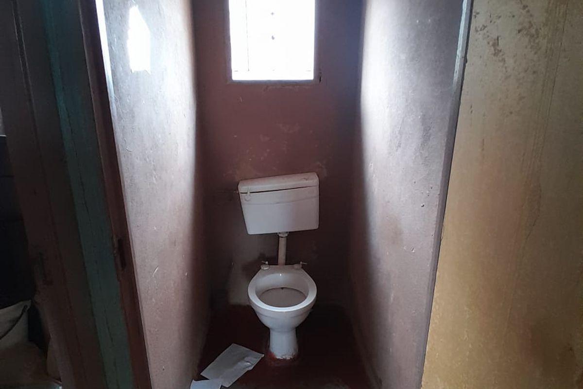 A small, basic bathroom featuring a standard toilet and window, currently requiring significant cosmetic updates and refurbishment to improve its condition.