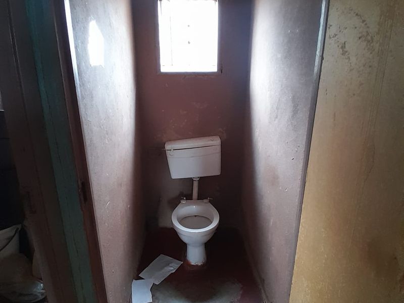 A small, basic bathroom featuring a standard toilet and window, currently requiring significant cosmetic updates and refurbishment to improve its condition.