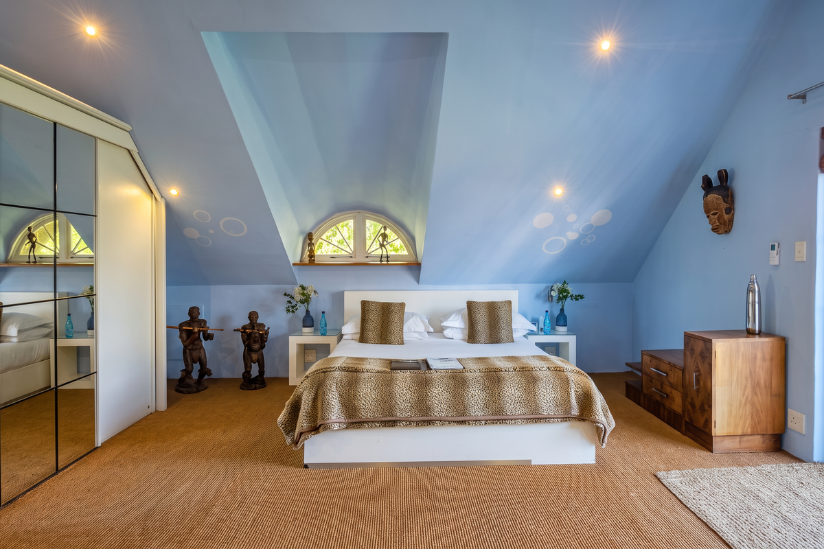 A well-lit bedroom featuring a vaulted ceiling, built-in mirrored wardrobe, arched window, and direct access to an outdoor area through a glass sliding door.