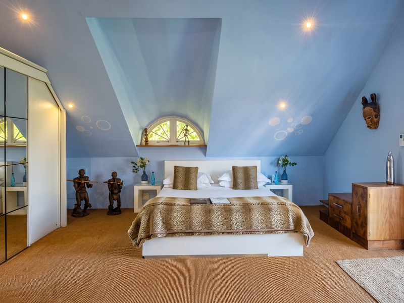 A well-lit bedroom featuring a vaulted ceiling, built-in mirrored wardrobe, arched window, and direct access to an outdoor area through a glass sliding door.