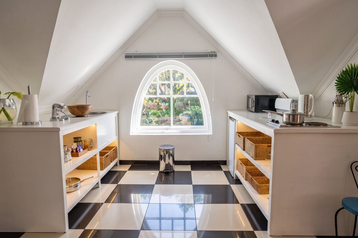 A bright, attic-style kitchen featuring custom white cabinetry, a central arched window, and a classic black and white checkered tiled floor.