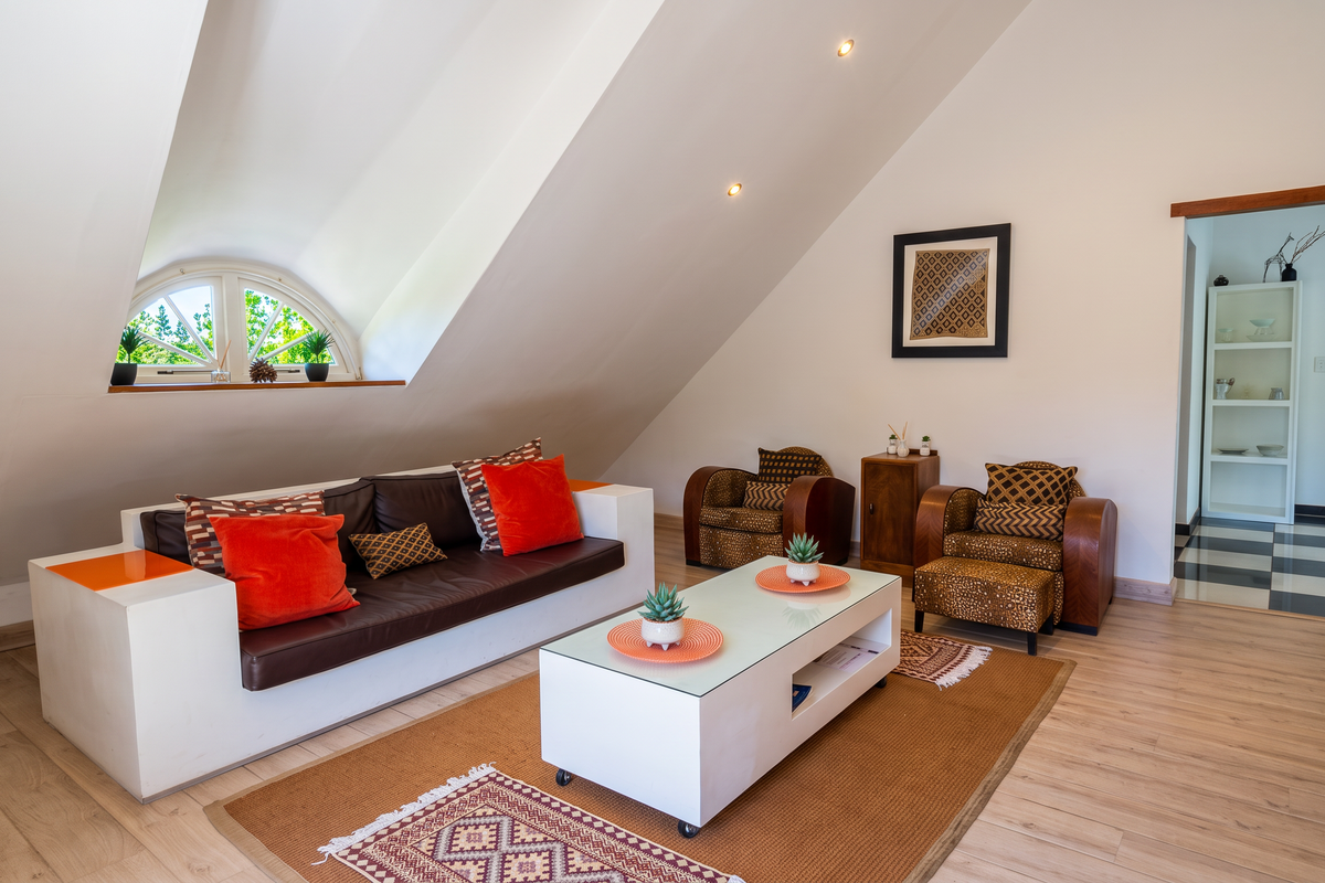 A bright living room featuring a unique sloped ceiling, an arched window, and modern laminate flooring, creating a cozy and inviting atmosphere.