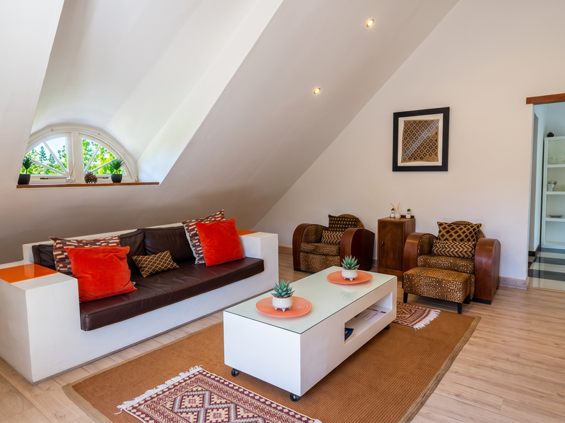 A bright living room featuring a unique sloped ceiling, an arched window, and modern laminate flooring, creating a cozy and inviting atmosphere.