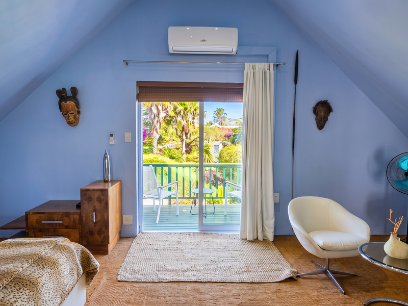 A spacious bedroom featuring a vaulted ceiling, split-system air conditioning, and direct access to a private balcony with garden views.