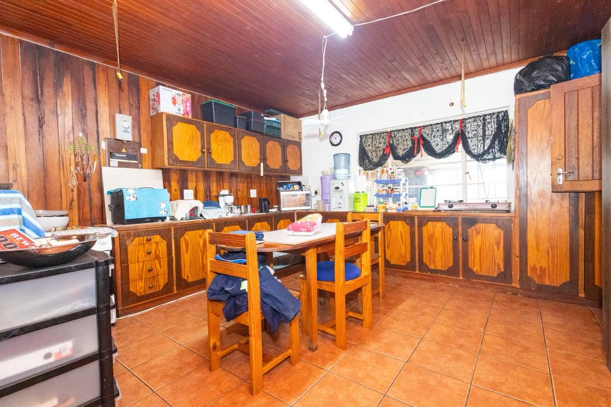 A dated kitchen featuring extensive wooden wall paneling, wooden cabinetry, and tiled flooring, offering significant potential for a modern renovation.