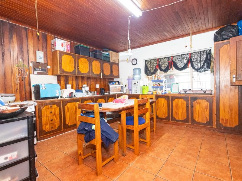 A dated kitchen featuring extensive wooden wall paneling, wooden cabinetry, and tiled flooring, offering significant potential for a modern renovation.