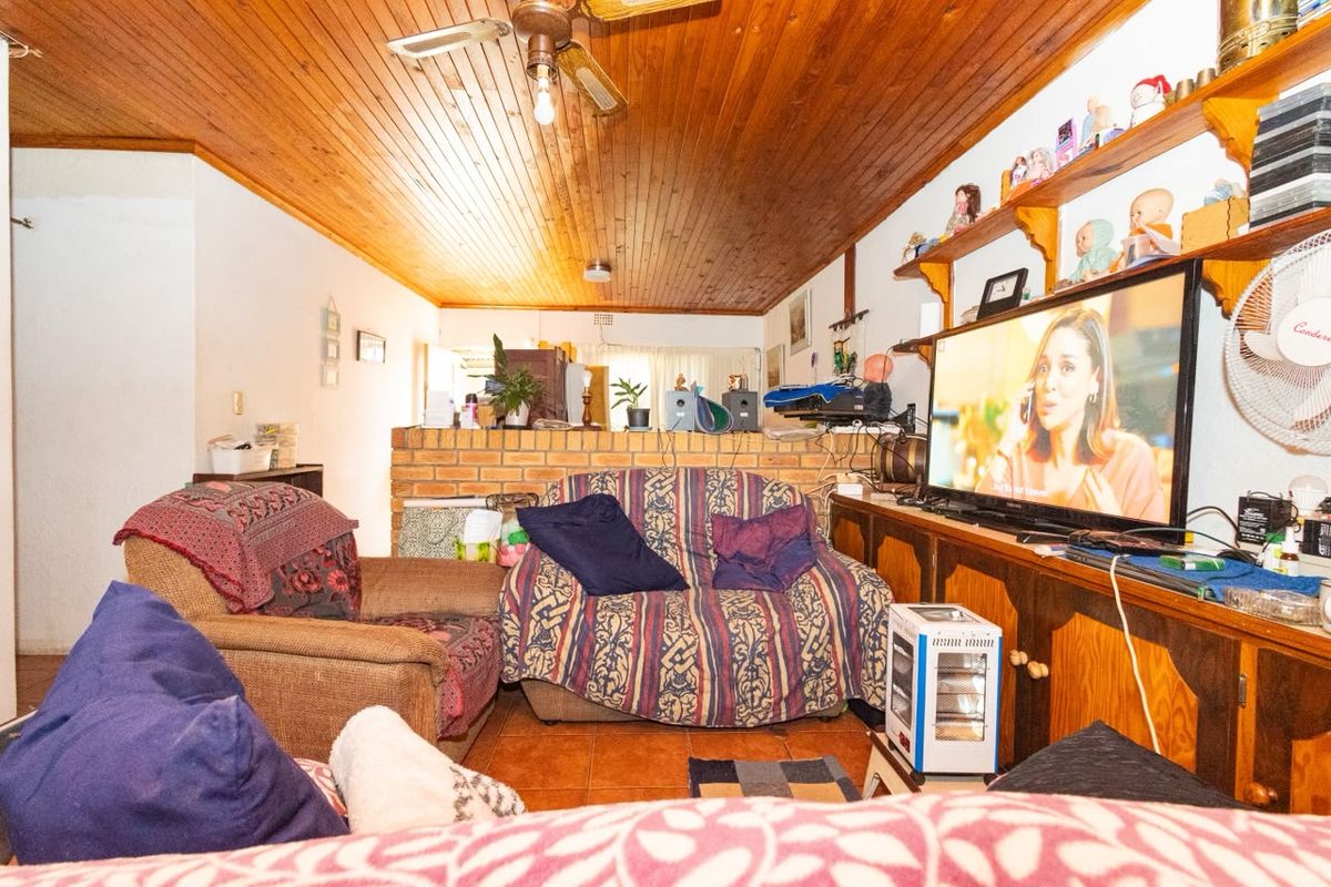 Living room featuring a timber tongue and groove ceiling, ceiling fan, tiled flooring, and a brick partition wall with built-in cabinetry.