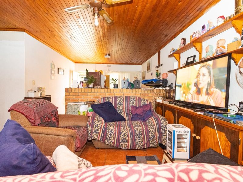 Living room featuring a timber tongue and groove ceiling, ceiling fan, tiled flooring, and a brick partition wall with built-in cabinetry.