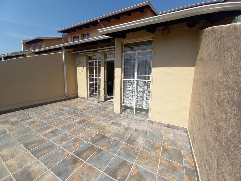 A paved outdoor patio area featuring tiled flooring, security gates, and direct access to the interior living space.