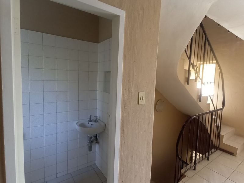 A hallway area featuring a small wall-mounted basin with tiled splashback, adjacent to a staircase with a metal balustrade.