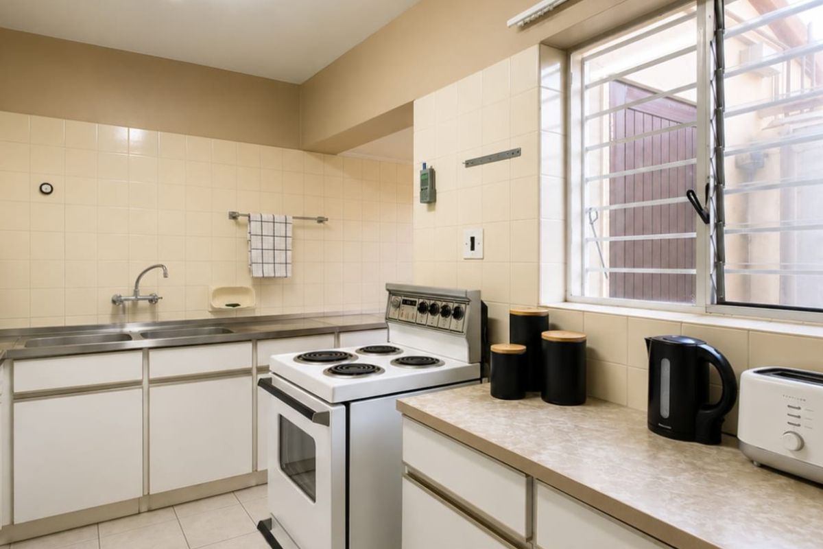 A functional kitchen featuring white cabinetry, laminate countertops, a tiled splashback, and a freestanding electric stove with security bars on the window.