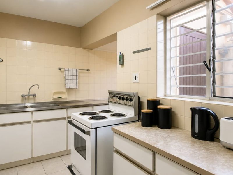 A functional kitchen featuring white cabinetry, laminate countertops, a tiled splashback, and a freestanding electric stove with security bars on the window.