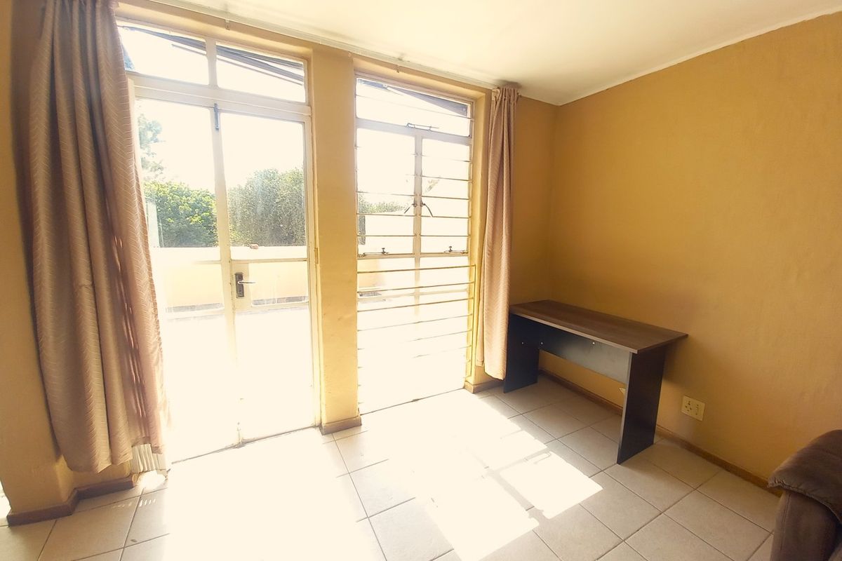 A bright, tiled bedroom featuring large windows with security bars and direct access to an outdoor area.