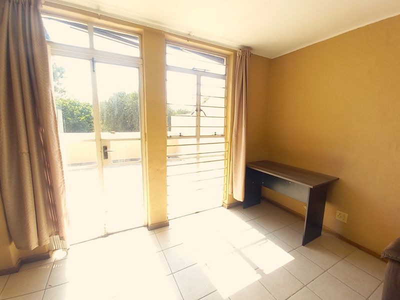 A bright, tiled bedroom featuring large windows with security bars and direct access to an outdoor area.