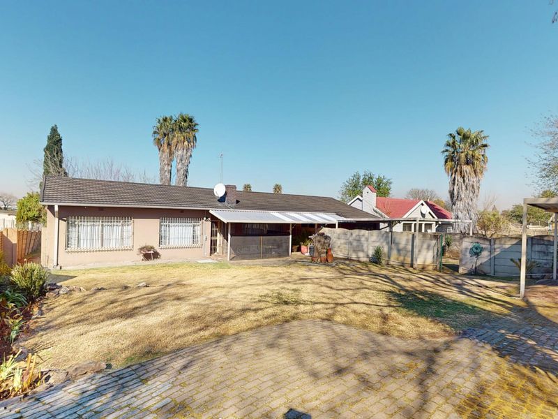 Rear view of the property featuring a spacious backyard, paved driveway, carport, and a covered patio area with security bars on windows.