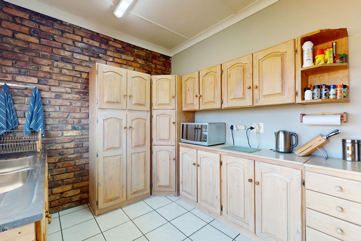Kitchen featuring exposed brick wall, tiled flooring, and extensive built-in wooden cabinetry with a stainless steel double sink.