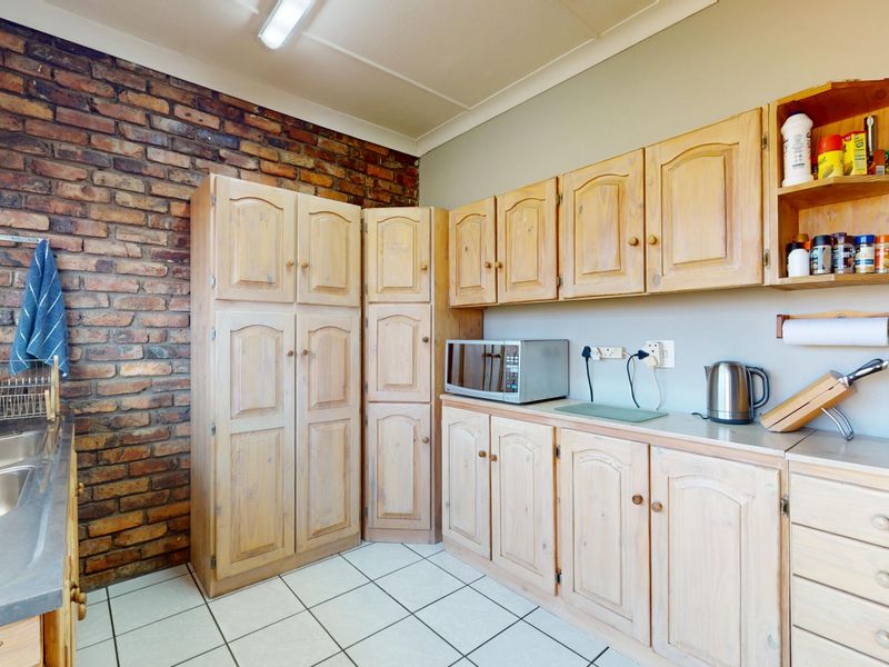 Kitchen featuring exposed brick wall, tiled flooring, and extensive built-in wooden cabinetry with a stainless steel double sink.