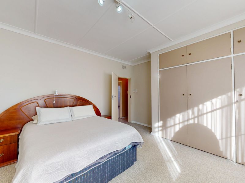 A spacious bedroom featuring neutral walls, carpeted flooring, and extensive built-in cupboard storage with overhead compartments.