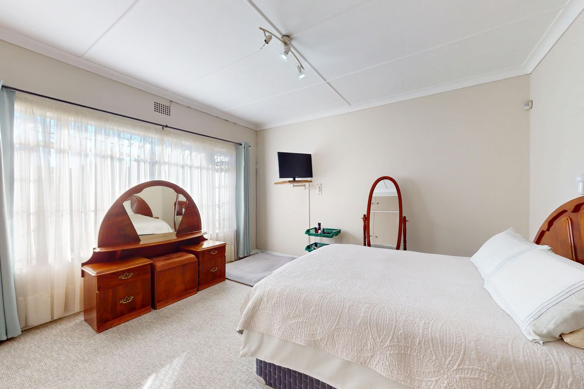 A well-lit bedroom featuring neutral wall tones, carpeted flooring, and large windows with curtain rails, offering a comfortable and functional living space.