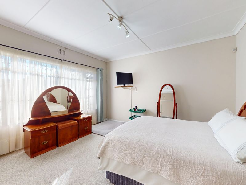A well-lit bedroom featuring neutral wall tones, carpeted flooring, and large windows with curtain rails, offering a comfortable and functional living space.