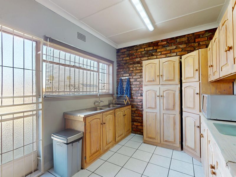 A functional scullery area featuring exposed brickwork, wooden cabinetry, a stainless steel sink, and tiled flooring with direct access to the exterior.