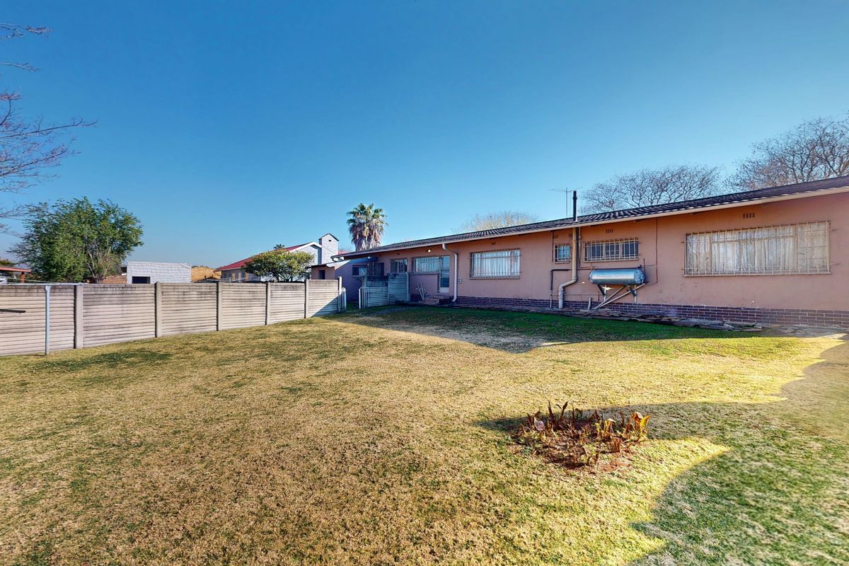Spacious rear garden featuring a large lawn area, perimeter precast concrete walling, and a rear building elevation with a solar water heater.