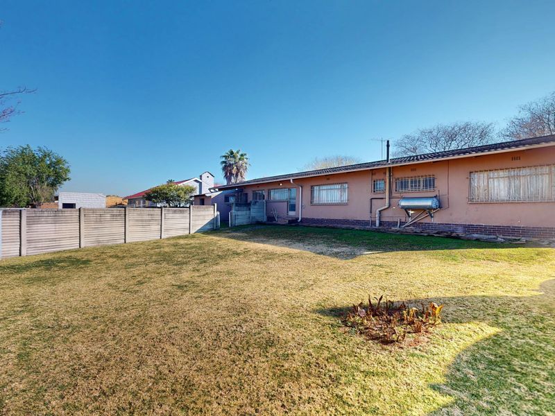 Spacious rear garden featuring a large lawn area, perimeter precast concrete walling, and a rear building elevation with a solar water heater.