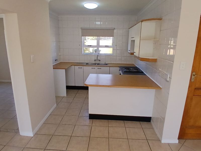 A functional kitchen featuring built-in cabinetry, laminate countertops, a double basin sink, and an electric hob with tiled splashbacks and flooring.