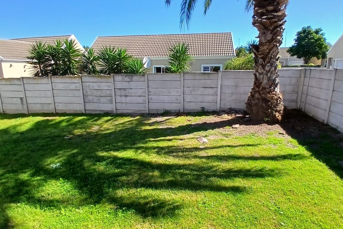 A private rear garden featuring a lawn area enclosed by a precast concrete boundary wall and a mature palm tree.