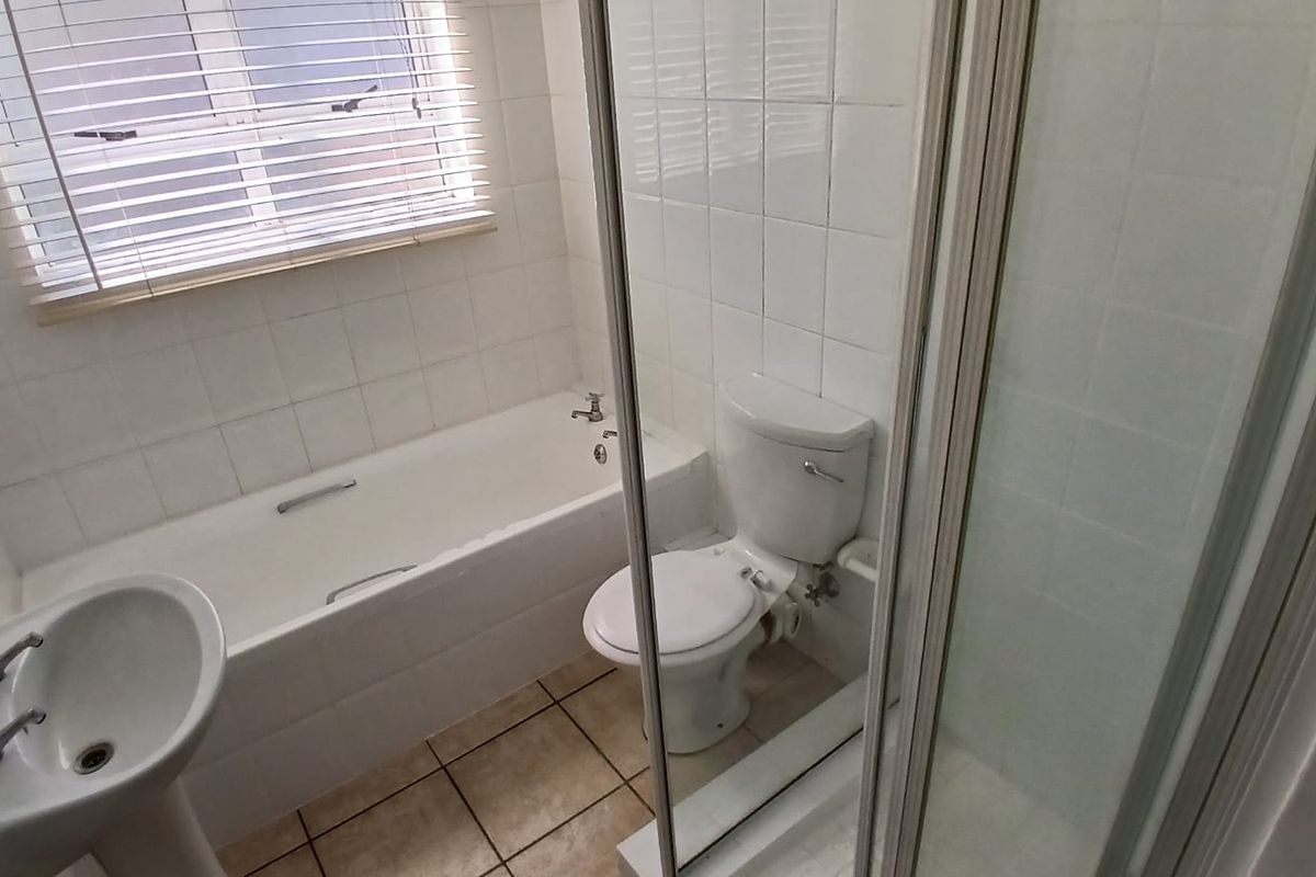 A functional bathroom featuring a pedestal basin, built-in bathtub, and a separate shower enclosure with white wall tiling and neutral floor tiles.