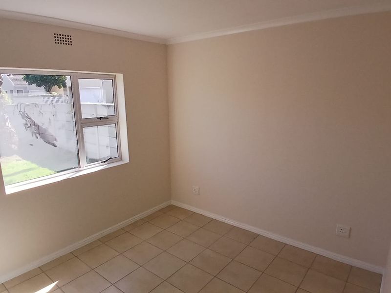 A clean, empty bedroom featuring neutral wall tones, tiled flooring, and an aluminium-framed window providing natural light.
