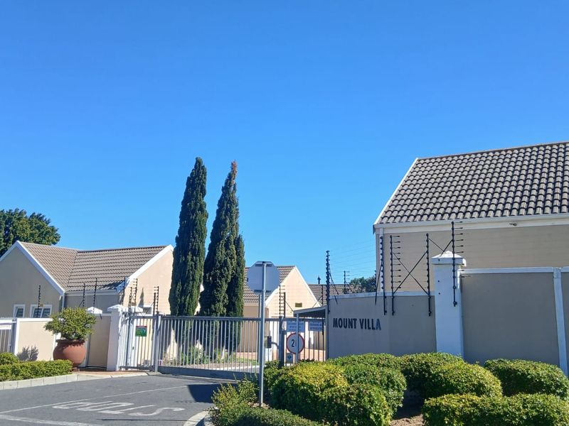 Front entrance view of Mount Villa complex featuring a secure gated access point, perimeter wall with electric fencing, and well-maintained landscaping.