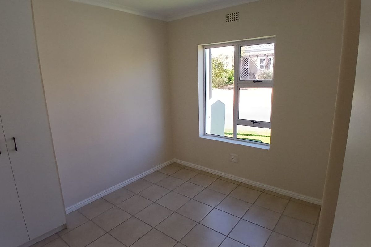 A clean, empty bedroom featuring neutral tiled flooring, built-in cupboards, and a window providing natural light.