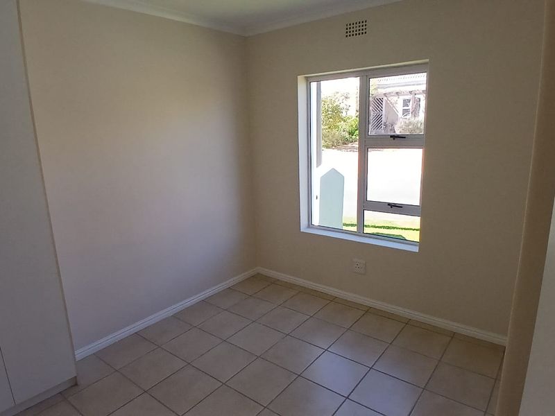 A clean, empty bedroom featuring neutral tiled flooring, built-in cupboards, and a window providing natural light.