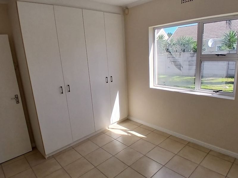 A bright, empty bedroom featuring neutral tiled flooring and ample built-in cupboard storage space.