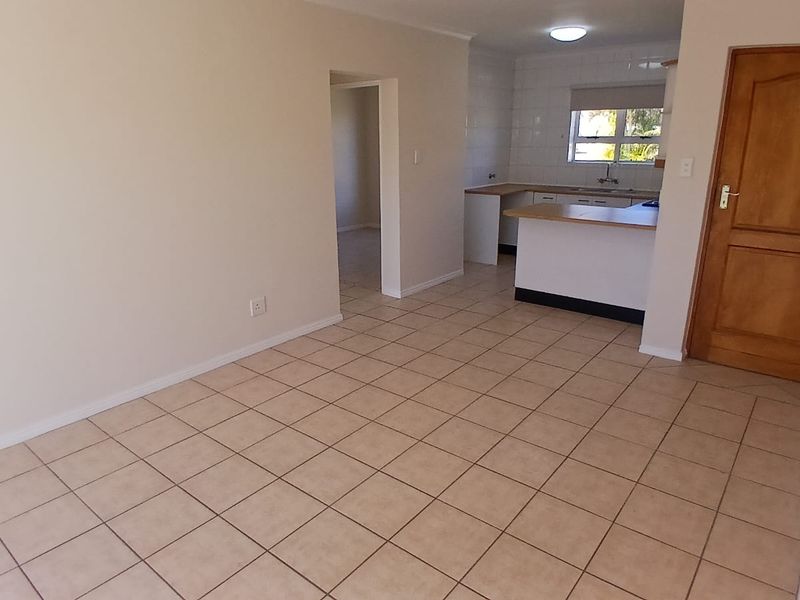 An open-plan living and kitchen area featuring neutral tiled flooring, functional kitchen cabinetry with countertops, and a wooden interior door.