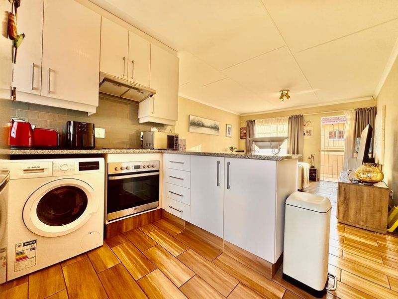 Open-plan kitchen and living area featuring modern white cabinetry, granite countertops, built-in oven, and tiled flooring with direct access to a balcony.