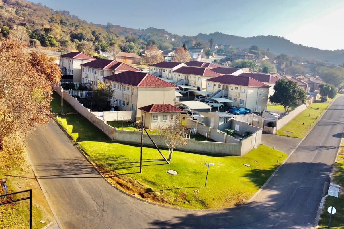 Aerial view of a residential apartment complex featuring multiple buildings with tiled roofs, paved driveways, carports, and surrounding landscaped grounds.