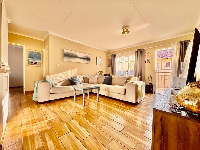 A bright and inviting living room featuring wood-look tiled flooring, neutral walls, and direct access to a balcony through a sliding glass door.
