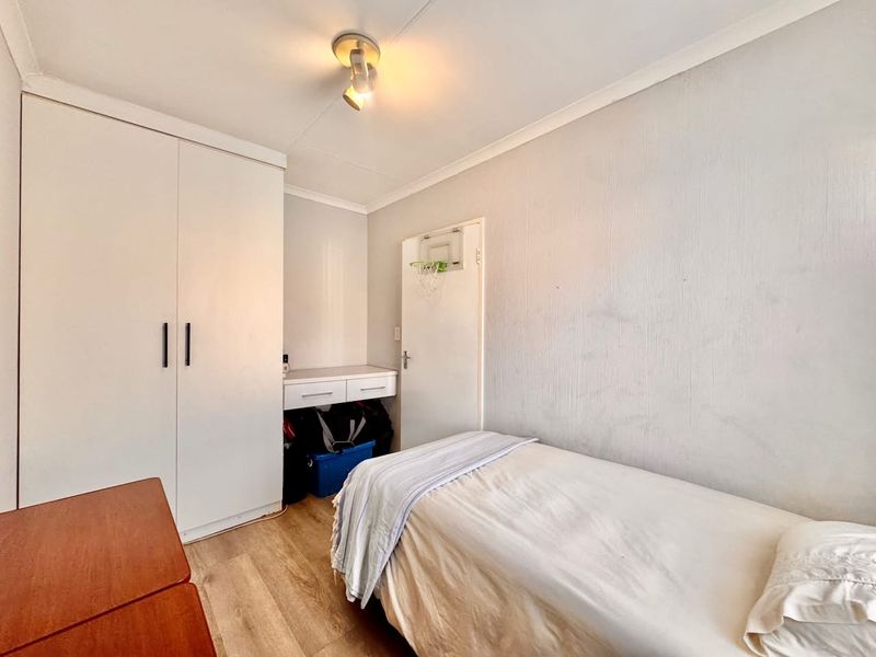 A functional bedroom featuring built-in wardrobe storage, a compact built-in desk, and laminate flooring.