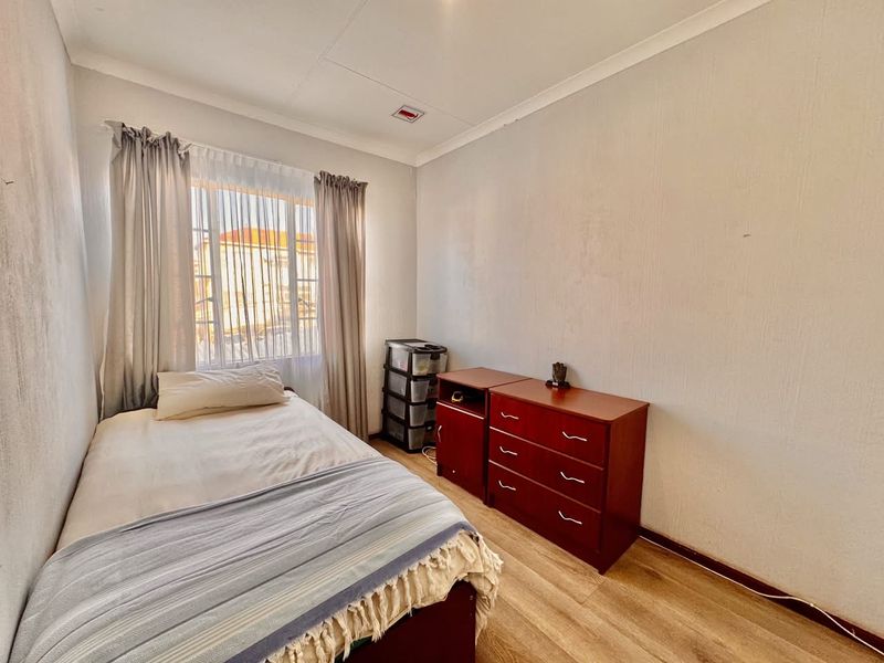 A bedroom featuring laminate flooring and a window with curtains. The room requires cosmetic updates to the walls and ceiling.