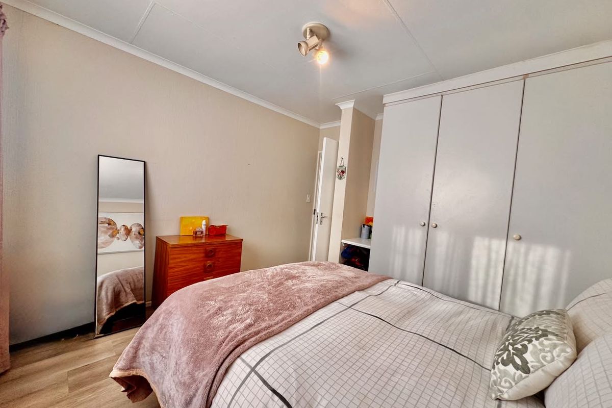 A functional bedroom featuring built-in cupboards, laminate flooring, and a ceiling-mounted spotlight fixture, offering a neutral base for personalization.