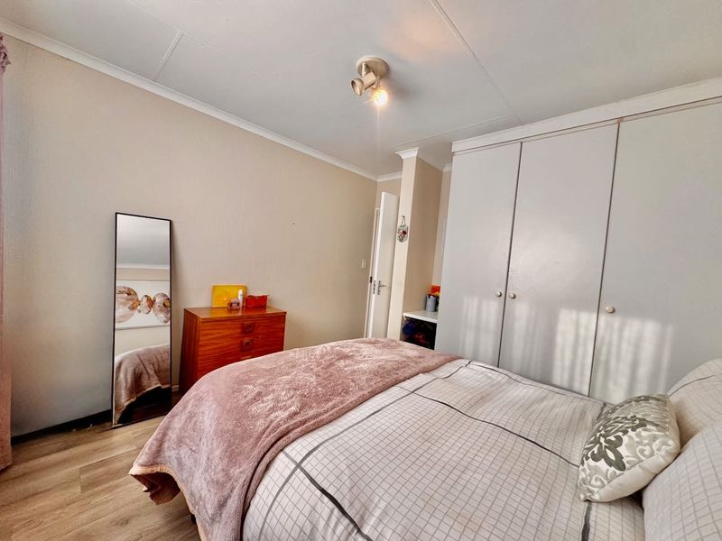 A functional bedroom featuring built-in cupboards, laminate flooring, and a ceiling-mounted spotlight fixture, offering a neutral base for personalization.