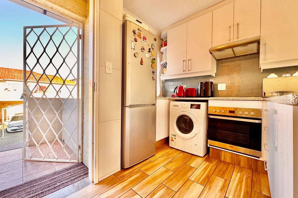 Compact kitchen featuring built-in cabinetry, integrated oven, extractor fan, and tiled backsplash, with direct access to an outdoor area via a security gate.