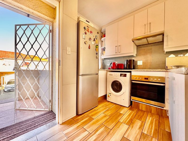 Compact kitchen featuring built-in cabinetry, integrated oven, extractor fan, and tiled backsplash, with direct access to an outdoor area via a security gate.